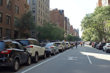 Fototapeta premium Row of parked cars lining a busy city street in sunlight