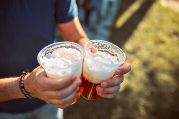 Person holding beer cup outdoors on a sunny day.