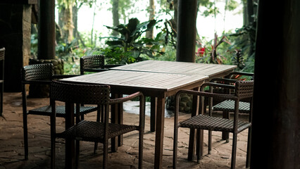 Empty rustic outdoor dining area with wooden table and chairs in a lush, natural, and peaceful setting.