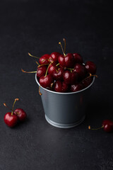 Juicy ripe fresh cherries with water drops in a miniature bucket on a black background. Seasonal fruits, harvest. Selective focus, close-up.