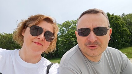 Happy middle-aged couple wearing sunglasses taking a selfie outdoors on a sunny day, smiling together in a green park environment