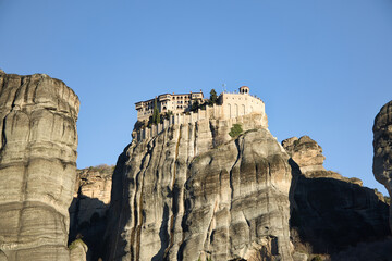 Meteora’s monasteries perch on rocky cliffs, lit by soft afternoon winter sun, blending nature...