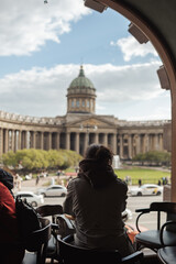 A person sits in a cafe, gazing out at Kazan Cathedral in St Petersburg, surrounded by lush...