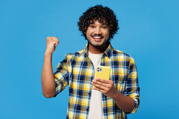 Young happy Indian man he wearing yellow checkered shirt casual clothes hold in hand use mobile...