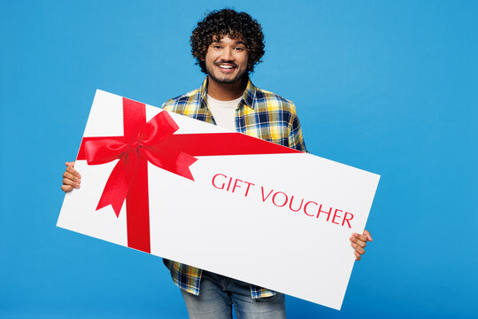 Young surprised Indian man he wear yellow checkered shirt casual clothes hold big huge gift certificate coupon voucher card for store isolated on plain blue cyan background studio. Lifestyle concept. - Powered by Adobe
