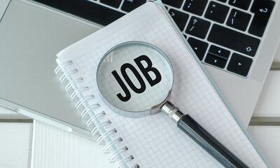 A magnifying glass is on top of a notebook with the word Job written on it