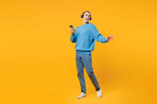 Full body young middle eastern man wear blue sweatshirt casual clothes listen to music in headphones use mobile cell phone isolated on plain yellow orange background studio portrait Lifestyle concept - Powered by Adobe