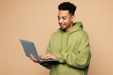 Young smart IT man of African American ethnicity wear green hoodie casual clothes hold use work on...