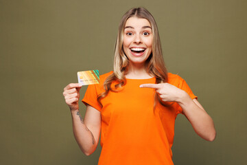 Young smiling woman she wears orange t-shirt casual clothes hold in hand point index finger on mock...
