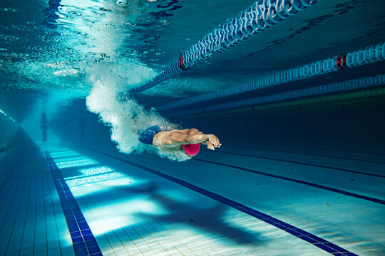 Fototapeta Swimmer in motion captured mid-dive in a pool, releasing bubbles and energy. Dramatic shadow resembling a shark looms beneath. Concept of transition, transformation, and deep inner state