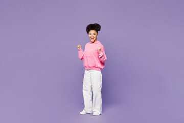 Full body young woman of African American ethnicity wear pink hoodie casual clothes doing winner...