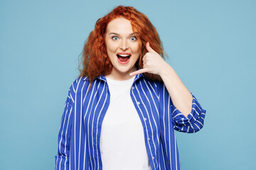 Young surprised ginger woman she wears shirt t-shirt casual clothes doing phone gesture like says call me back isolated on plain pastel light blue cyan background studio portrait. Lifestyle concept.