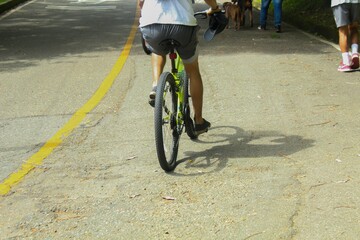 A young man dressed in dark pants and a comfortable pastel-colored t-shirt is riding a bicycle,...