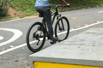 A young man dressed in dark pants and a comfortable pastel-colored t-shirt is riding a bicycle,...