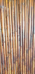 A close-up image of vertically aligned bamboo poles, showcasing their natural brown hues, smooth...
