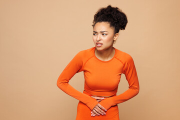 Young strong fitness trainer sporty woman wearing orange clothes spend time in home gym put hands...