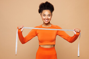 Young strong fitness trainer instructor sporty woman sportsman wears orange clothes spend time in home gym hold show measuring tape isolated on plain beige background. Workout sport fit abs concept.