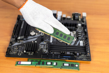 A single hand, protected by a white glove, holds a green RAM (Random Access Memory) module above a...