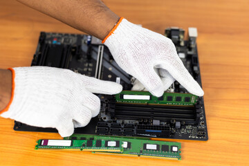 A close-up, high-angle shot of gloved hands carefully inserting a green RAM (Random Access Memory)...