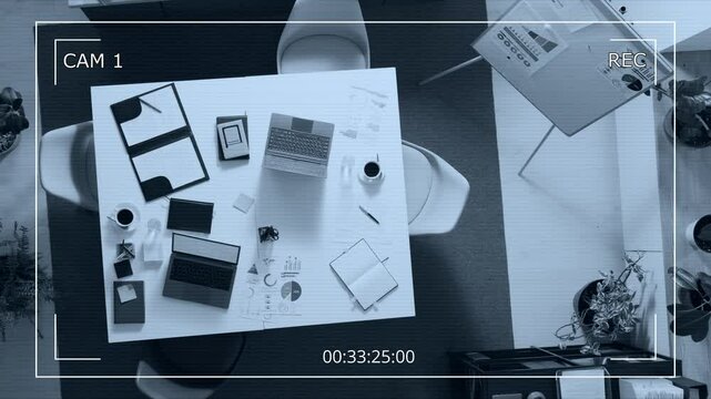 High angle surveillance camera shot of empty office with whiteboard, large office table featuring laptops, folder with documents, coffee cups and notebooks
