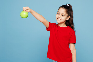 Little kid girl 8-9 years old wears red t-shirt have fun hold eat give green apple look aside...