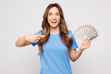 Young woman wearing blue t-shirt casual clothes hold in hand point finger on fan of cash money in...