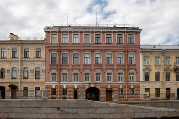 Fototapeta premium Beautiful buildings line the canal in St. Petersburg, displaying distinct architectural styles and colors under a partly cloudy sky, evoking history.