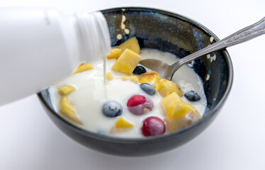 A person pouring kefir natural yogurt into a bowl with mixed fruits.