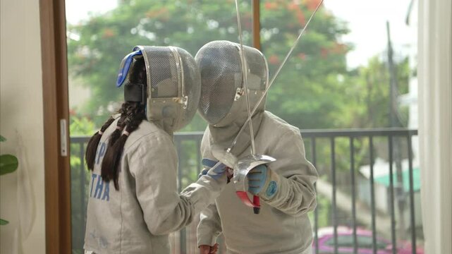 Before the tournament day, a boy and girl dressed in fencing gear are rehearsing in gym