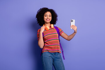 Young woman taking a selfie against a vibrant purple background showcasing casual fashion with a...