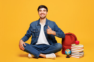 Full body young smiling happy boy student wears denim casual clothes sit near backpack bag hold...