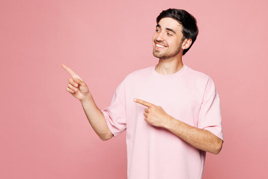 Young smiling happy Caucasian man he wear t-shirt casual clothes pointing index finer aside indicate on workspace area isolated on plain pastel light pink background studio portrait Lifestyle concept