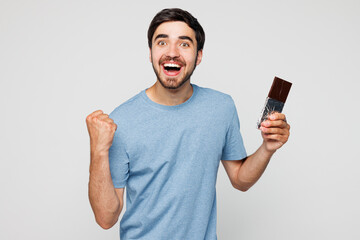 Young happy man he wear blue t-shirt casual clothes hold in hand eat chocolate bar do winner...