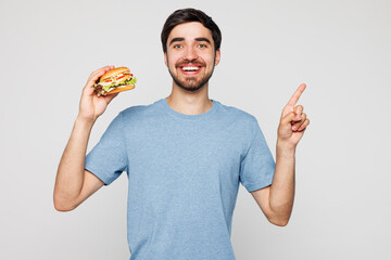Young man he wear blue t-shirt casual clothes hold eat burger point index finger aside on blank...
