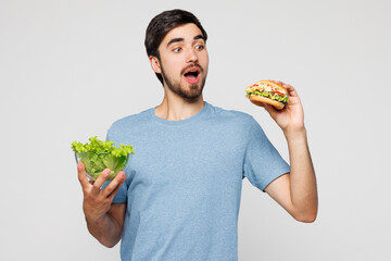 Young shocked man he wear blue t-shirt casual clothes hold lettuce salad choose vegetables or...