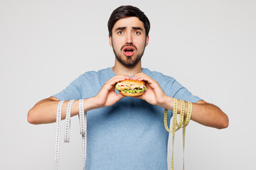 Young shocked sad man wear blue t-shirt casual clothes, tied hands with measure tape hold eat...