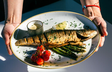 Grilled fish with asparagus, cherry tomatoes, lemon, and sauce on a plate
