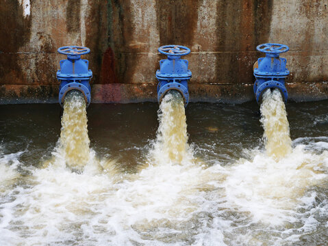 Industrial drainage system with five blue pipes discharging water into a reservoir. Concept of water management, wastewater treatment, and environmental engineering, spillway