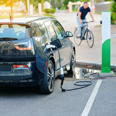 Car charging on rain-soaked pavement with power cable touching water puddle, about electric hazard...