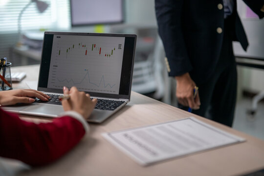 A person is typing on a laptop in front of a graph
