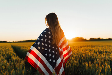 Young happy woman with American flag in a wheat field at sunset celebrate Independence day. 4th of July. Patriotic holiday, american day. Independence Day.