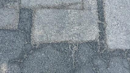 Rough asphalt surface of an old road with repair patches. Asphalt patchwork pattern.