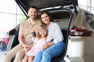 Happy family with keys sitting in car trunk in salon