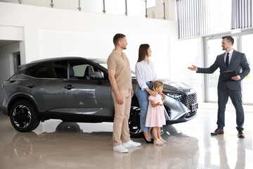 Salesman with clipboard showing new car to happy family in salon