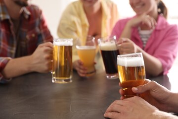 Friends with glasses of beer at grey table indoors, selective focus