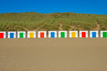 Multi-colored beach huts on Woolacombe Beach resting on sand in North Devon, UK
