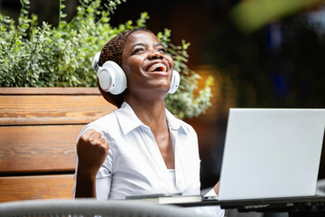 Elegant black African woman in business suit working on laptop computer and celebrating success in cafe bar.