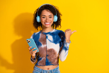 Happy young woman using her smartphone and listening to music with headphones on a vibrant yellow...