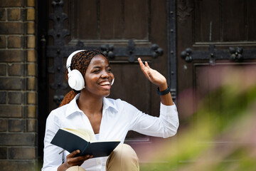 Happy black African student reading book and waving to his friend at college.