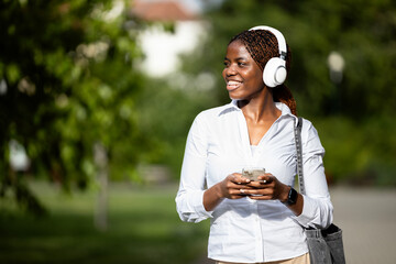 Smiling black African woman walking through the park and using smart phone.